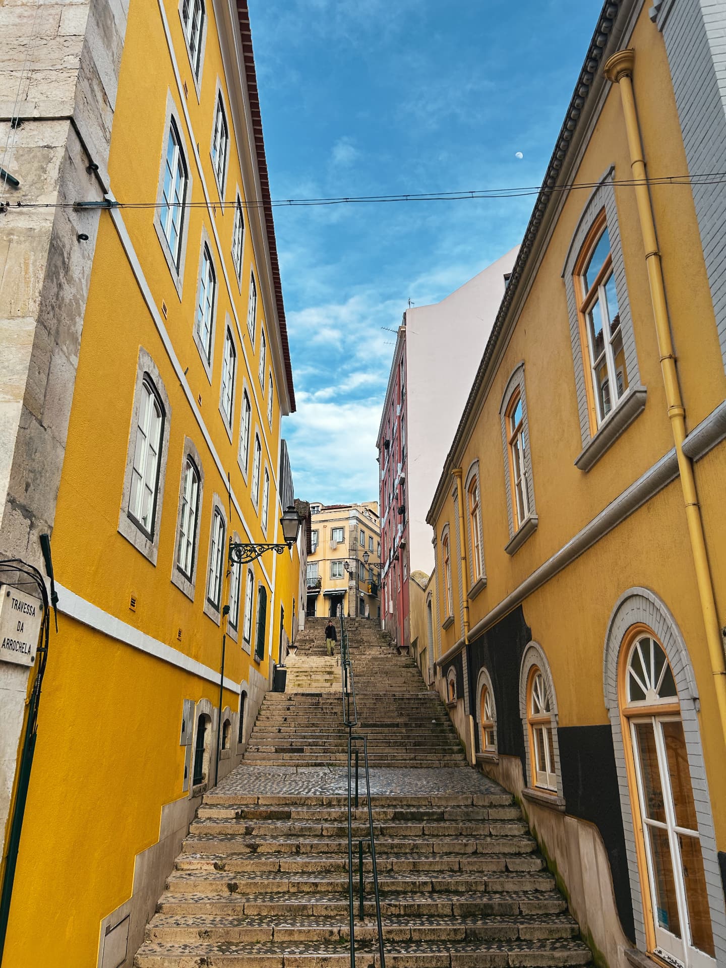 A stone stairway climbing between yellow buildings in Lisbon