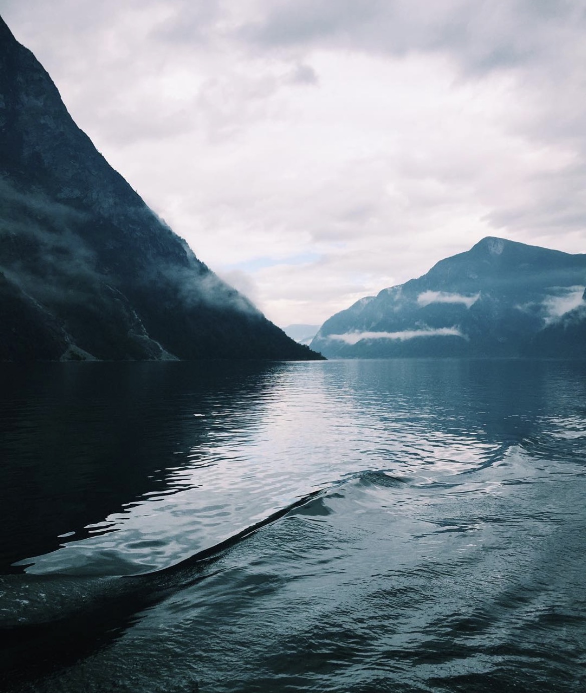 Still Norwegian fjord water beneath steep mountains and low cloud