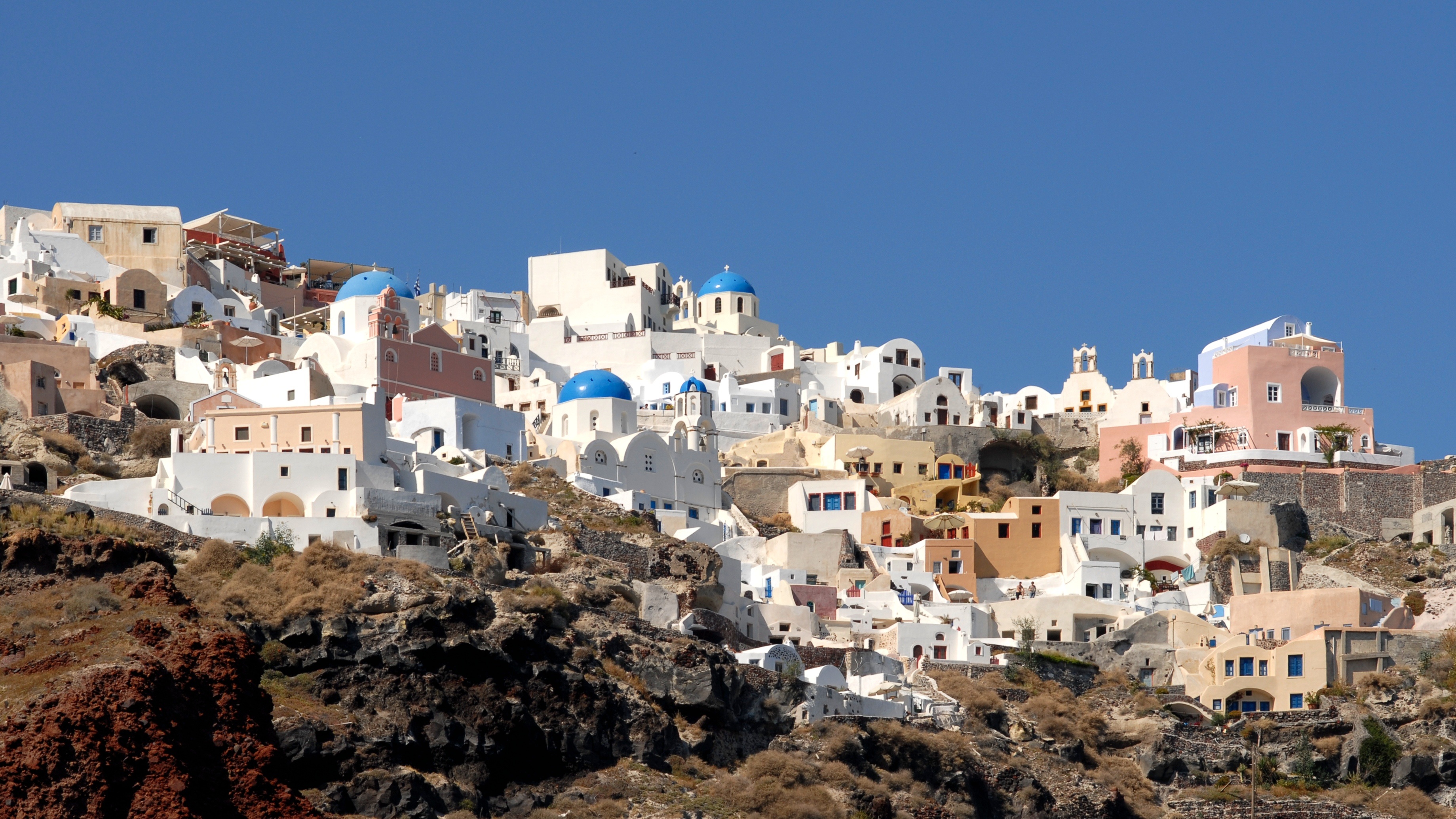 Blue-domed churches and whitewashed homes on Santorini's hillside beneath a clear sky