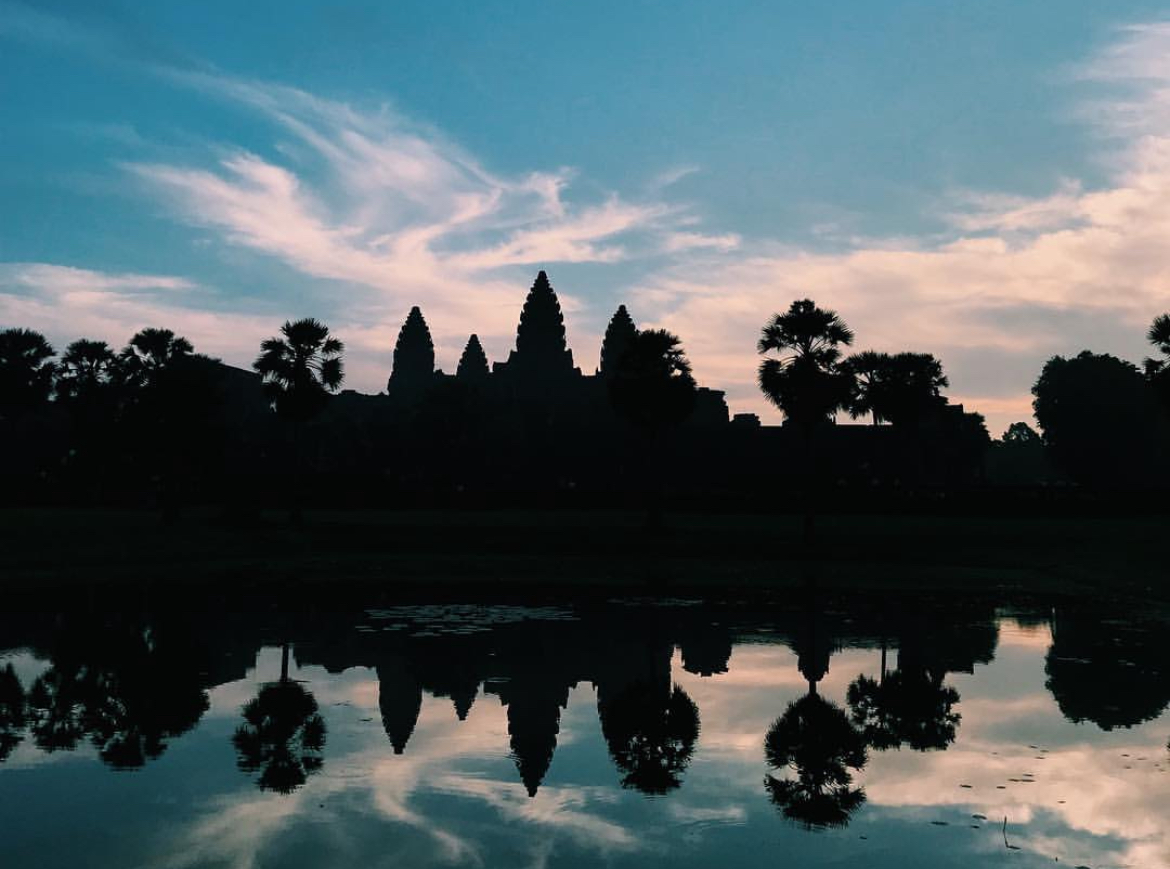 Angkor Wat's temple towers silhouetted above their full reflection beneath a pastel dawn sky